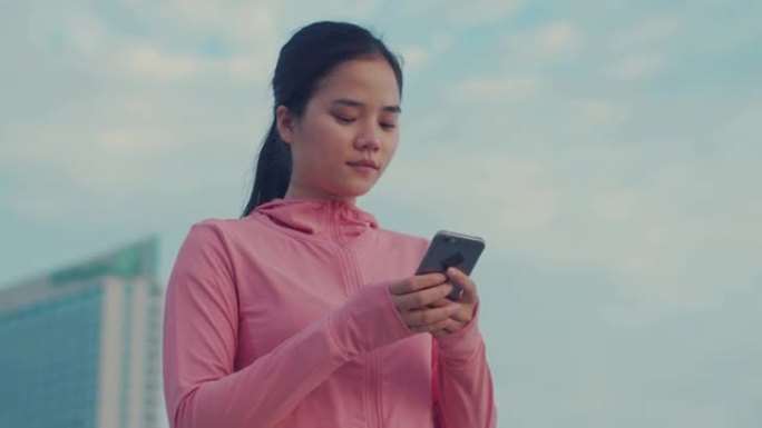 一名女运动员在海边跑步后休息时使用智能手机检查社交媒体供稿的肖像。女运动员站着休息时使用手机向朋友发
