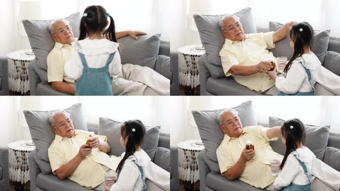 幸福的家庭小亚洲女儿带着药物和一杯水给生病的爷爷在家里的沙发上照顾，老人病人退休享受生活理念。