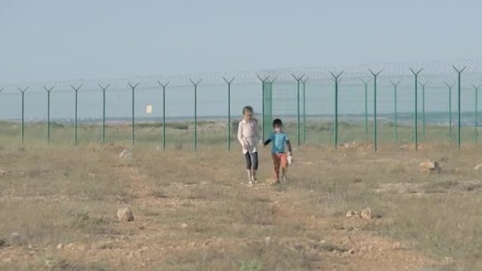 孩子们在难民营里走一条土路。概念移民危机可怜的男孩和他的妹妹需要帮助