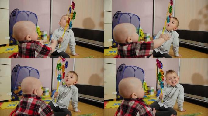小男孩在家为有趣的九个月大的弟弟吹玩具风车螺旋桨。