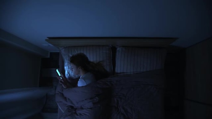 晚上躺在床上使用智能手机的女人。