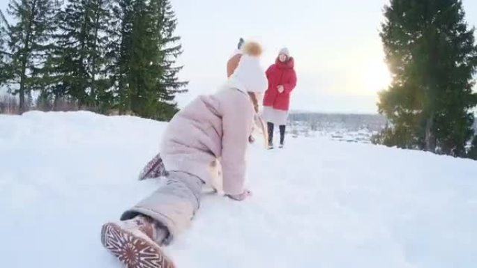 家人喜欢冬天。快乐可爱的女孩在雪原上爬行，父母在背景上