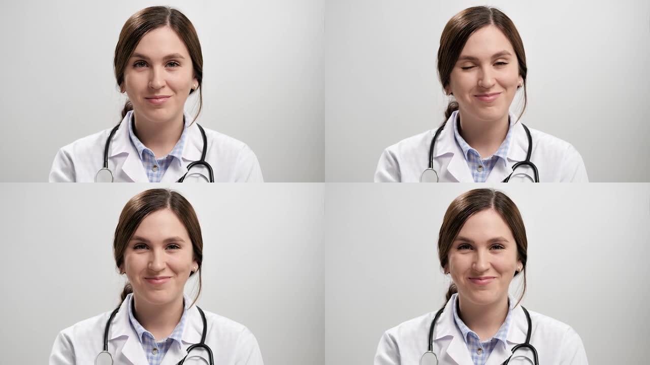 眨眼医生。灰色背景上的积极微笑女医生看着相机，用右眼嬉戏地眨眨眼。慢动作