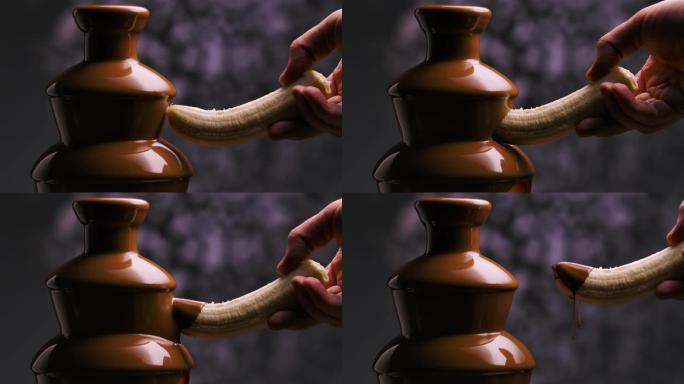 融化的牛奶巧克力在巧克力喷泉中流动。一个人的手将香蕉浸入从叶栅流下来的热液体巧克力中。火锅。甜点。派