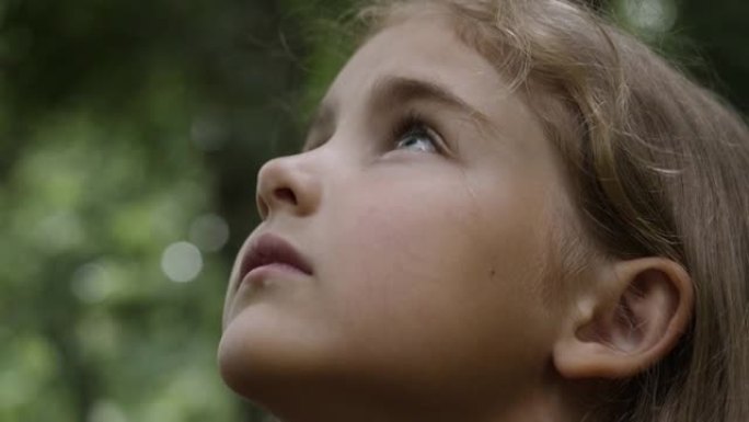 孩子抬头看着大自然的天空。肖像小女孩祈祷着带着希望和信念仰望天空，沉思的孩子脸，特写镜头。女孩仰望上