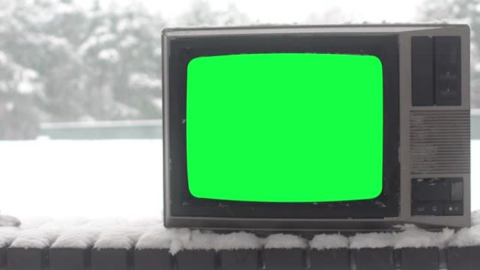 冬季长椅上绿屏的老式电视特写镜头被雪覆盖