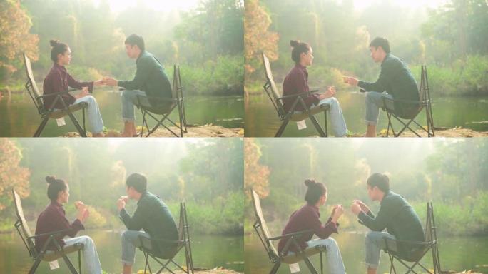 一对快乐的旅行者夫妇正在享受大自然的乐趣，早上在湖上喝咖啡，放松旅行度假的概念。