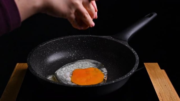 在煎锅里煎鸡蛋。女人准备早餐，按一下鸡蛋。高质量4k镜头