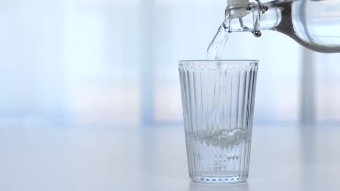 桌子上放了一杯透明的水，并在白色背景下将水瓶倒入房屋的玻璃中。
