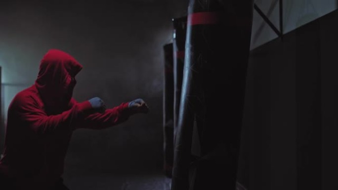 肖像，一个男性拳击手的剪影在一个黑暗的运动大厅的引擎盖上，烟雾弥漫。拳击手用手敲打出气筒，在战斗前练