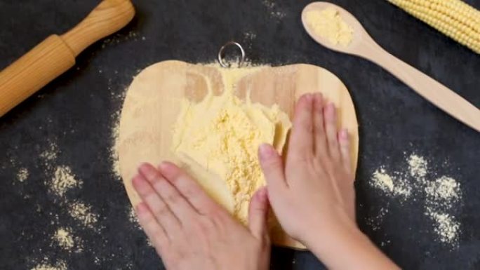 玉米粉在厨师手中的木板上，新鲜的玉米在黑暗的背景上。玉米生产产品的概念。从上方观看