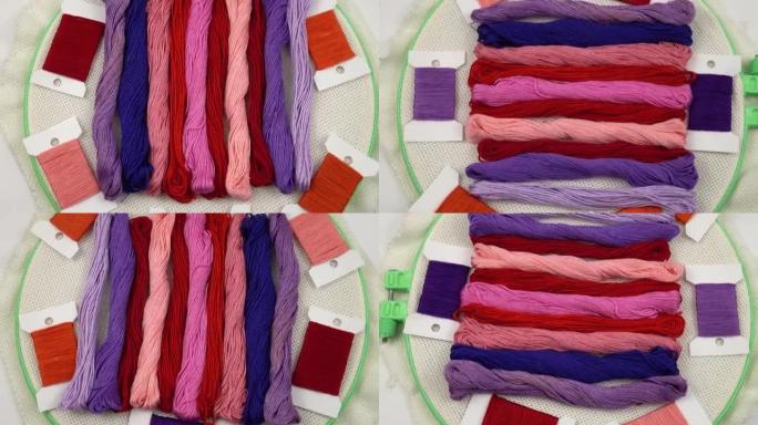 红色，粉红色和紫色调的绣花线排列在带有帆布的绣花环上