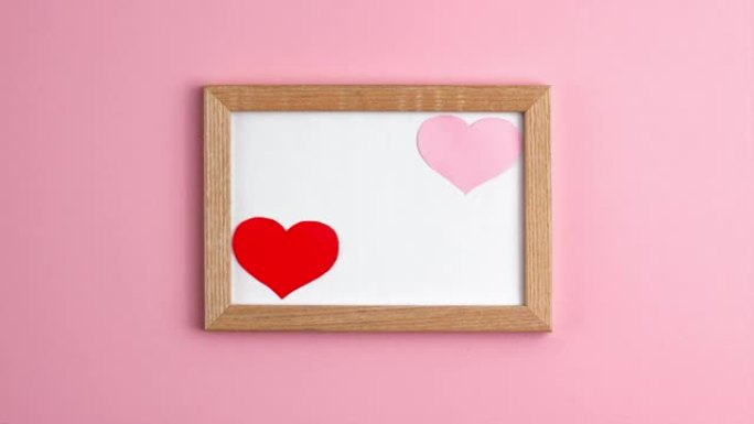 在中间的粉红色背景上的木制框架中的粉红色和红色纸心的停止运动动画。情人节，母亲节恋爱关系浪漫周年假期