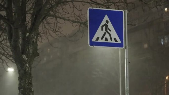 冬季傍晚降雪时，城市街道上的行人过街标志。特写。带有大雪和狂风的气旋
