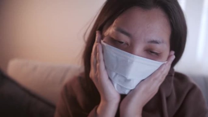 患有冠状病毒的年轻亚洲女性全身黑眼睛发冷，她用口罩和毯子在单独的客厅和检疫的沙发上保暖