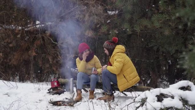 青年男女在冬日森林的炉火旁喝茶