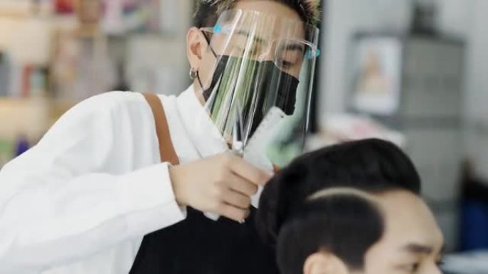 亚洲男子在理发店理发，美发师戴着医用口罩保护自己免受病毒。理发师在他的商店理发