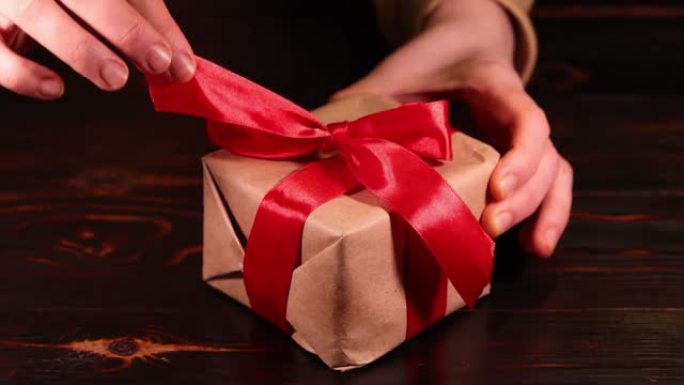 女人的手解开礼品盒上的红丝带。超级慢动作