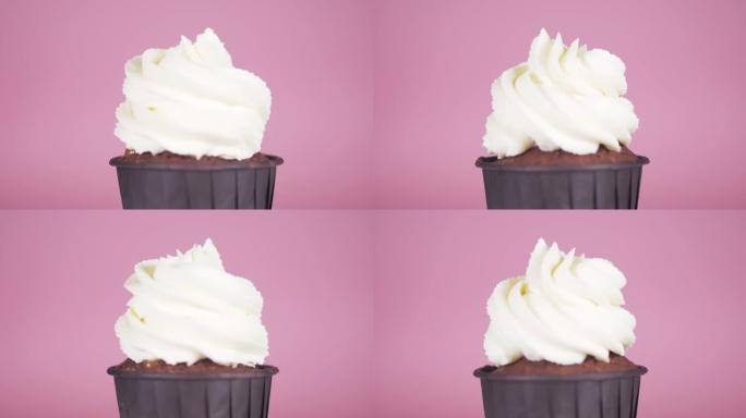 带有白色奶油的巧克力蛋糕在粉红色背景上沿其轴旋转