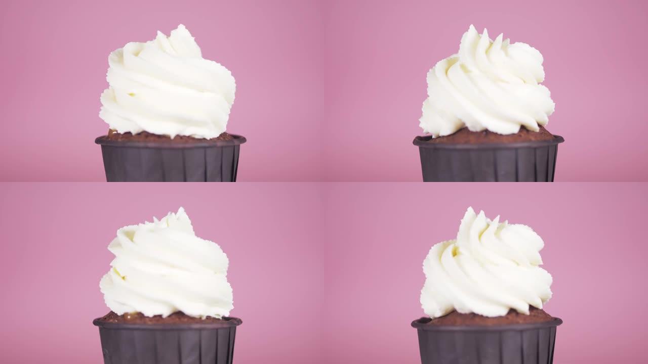 带有白色奶油的巧克力蛋糕在粉红色背景上沿其轴旋转