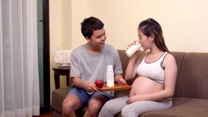 亚洲孕妇和丈夫呆在家里。妇女喝牛奶是为了怀孕的健康和健康。