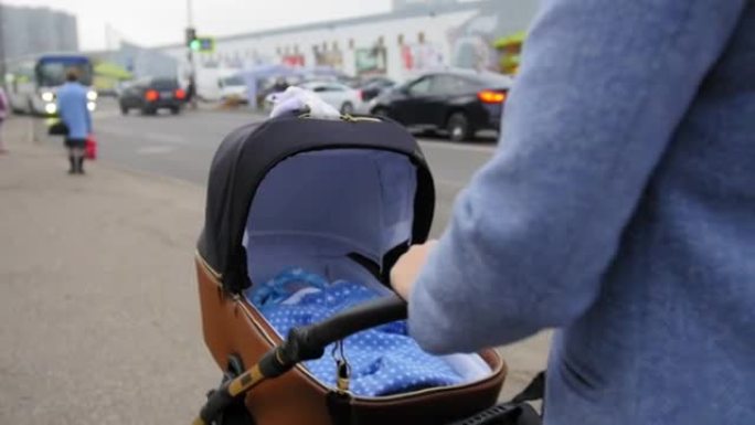 妈妈手握婴儿车把手，推婴儿车。母亲带着婴儿走在婴儿车里。特写镜头。