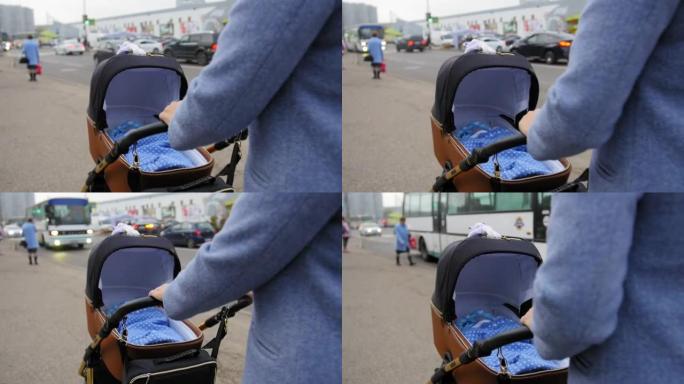 妈妈手握婴儿车把手，推婴儿车。母亲带着婴儿走在婴儿车里。特写镜头。