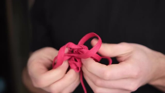 一个人解开一条红色的绳子，在模糊的背景上特写。背景是黑暗的。4K