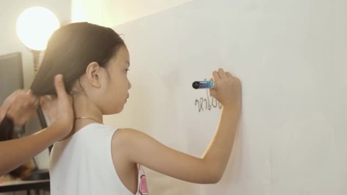 快乐的亚洲女孩在家上学的时候在白板上写答案，生活方式的概念。