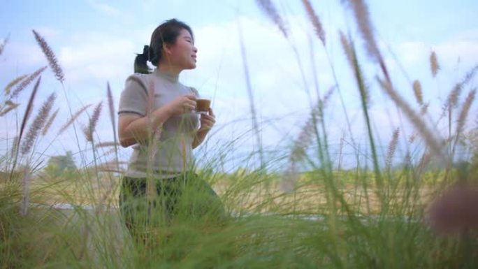 亚洲女性穿着白色连衣裙手持咖啡热饮晨间清新欢快卧室露台背景稻田自然花园和天空