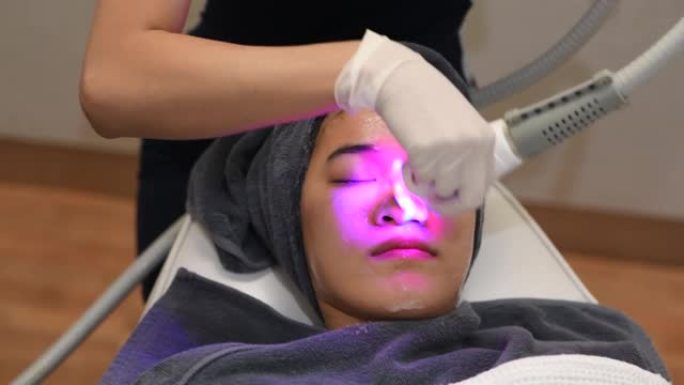 美容师使用激光疗法进行面部皮肤嫩肤的特写。美丽健康的女人脸在水疗沙龙里换肤。