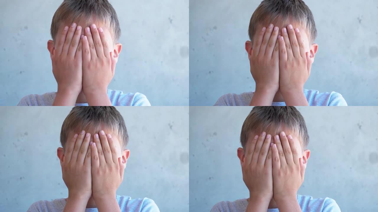 男孩抬起头来。孩子用手遮住脸。日间照明，灰色墙壁背景。4k视频