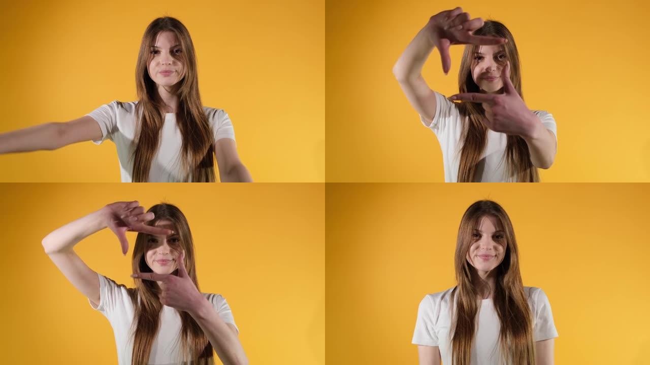 女孩用手指框住她的脸，假装拍照，橙色的工作室背景。特写