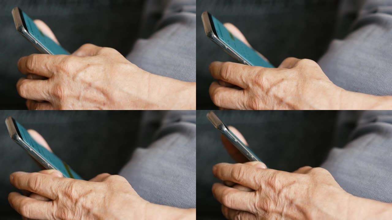 以智能手机为主题的老年人。一个老人的手的特写镜头，教你如何在移动设备上工作。养老金领取者笨拙地浏览电