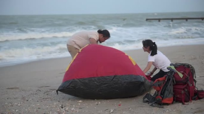 徒步旅行和露营概念。亚洲旅游夫妇帮助在海边搭帐篷。