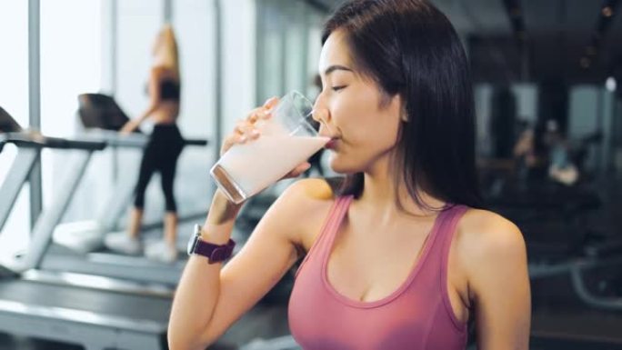 年轻的亚洲妇女在健身房锻炼后喝蛋白质奶昔