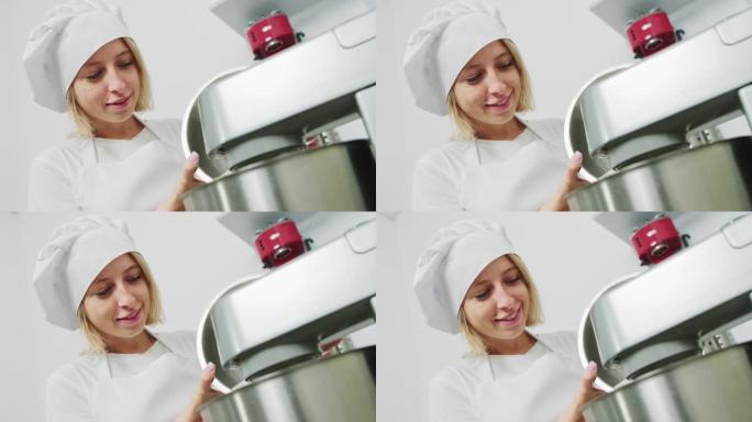 面对专业女厨师在现代银色厨房立式搅拌机的碗中加入糖，为马卡龙混合面团。美丽的女厨师揉面团。揉面搅拌机