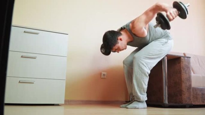 肌肉发达的运动员在家用哑铃靠在床上做运动。