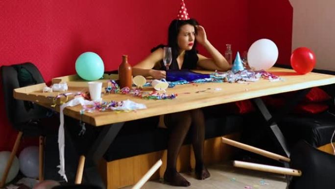 生日派对结束后，戴着红色擦口红和帽子的年轻女子早上在凌乱的房间里的桌子上醒来