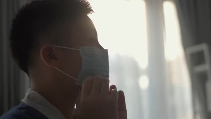 穿着制服的亚洲男生戴着口罩靠近窗户，在被封锁后准备返回学校新型冠状病毒肺炎。新年后上学的第一天。