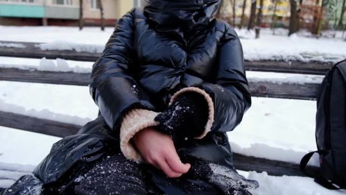 一个女人打扫，甩掉手套上的雪。她坐在白雪覆盖的长凳上。