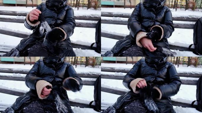 一个女人打扫，甩掉手套上的雪。她坐在白雪覆盖的长凳上。