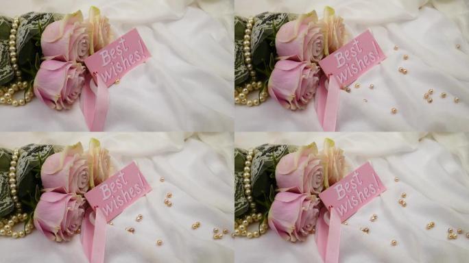 粉红色的珍珠珠子落在白色的丝绸上，一束玫瑰花和一张卡片上的祝福