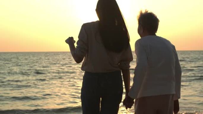 女人在海滩上牵着母亲的手。他们微笑着一起看着日落。