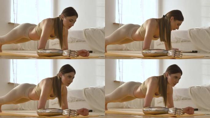 一个美丽的女人在运动上衣和绑腿上戴着仿生假肢站在房子的木板上，坐在瑜伽垫上，一边看着现代健身手表一边