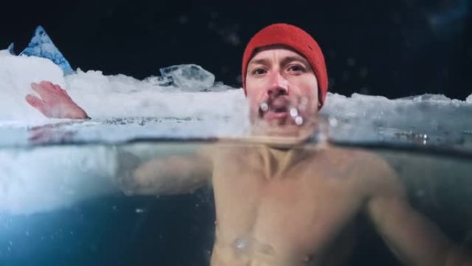 冬季游泳运动员肖像。年轻人晚上在冰冷的水中游泳，转头看着相机