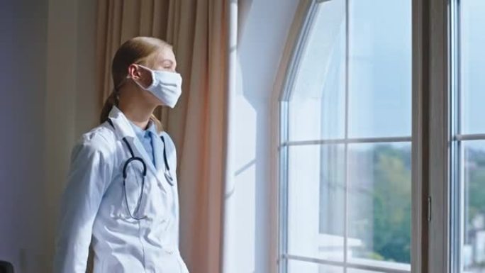 美丽的年轻女性医生戴着防护口罩，她休息了一下，透过全景窗户思考。在阿里·阿列克谢迷你上拍摄