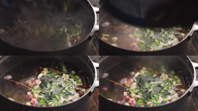 有人在往锅里倒食材，里面装满了红辣椒、青柠叶、大葱、高良姜和柠檬草。草药汤的配料。泰国菜菜单。