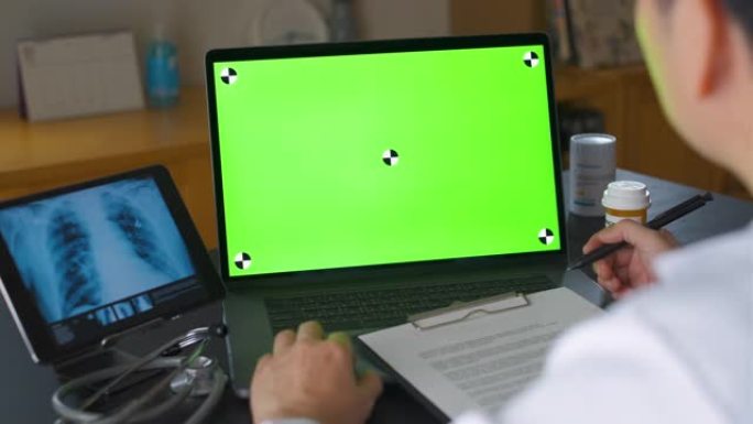 绿色屏幕，医生使用笔记本电脑并与患者进行视频通话，分析患者的肺部放射线图像或胸部x射线图像，向患者解