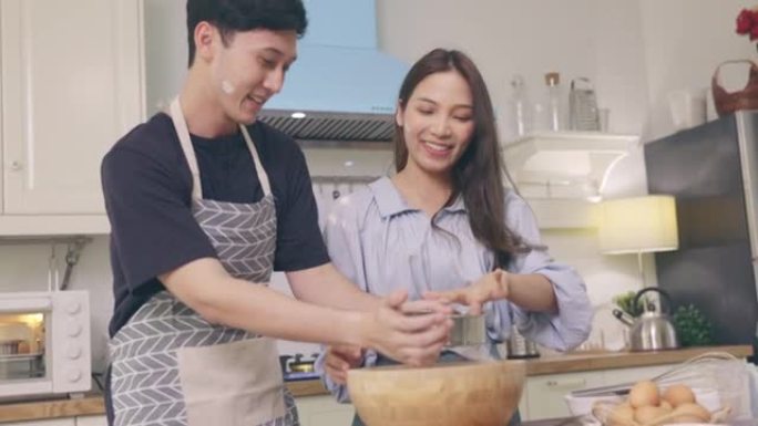 亚洲夫妇在家里的厨房里互相帮助，在浪漫的气氛中制作面包店。年轻女性用微笑和快乐的面孔帮助烹饪假期。